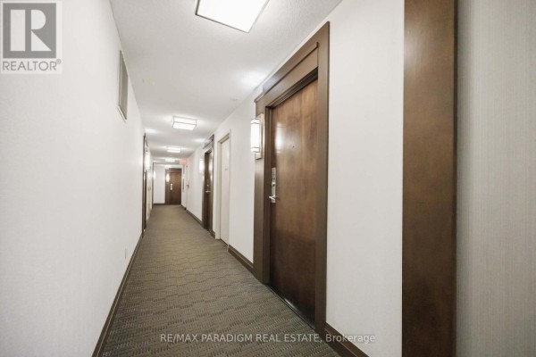 A long, carpeted apartment building hallway with numerous wooden doors and overhead lighting. - 1713 - 16 Yonge Street, Toronto