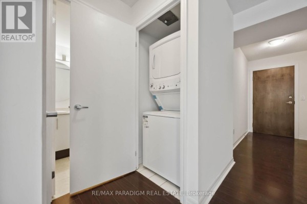 A compact laundry closet with a stacked white washer and dryer in an apartment hallway. - 1713 - 16 Yonge Street, Toronto