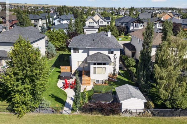 Aerial view of a backyard with a wooden deck, hot tub, red chairs, and a trampoline. - 1713 High Park Drive Nw, High River