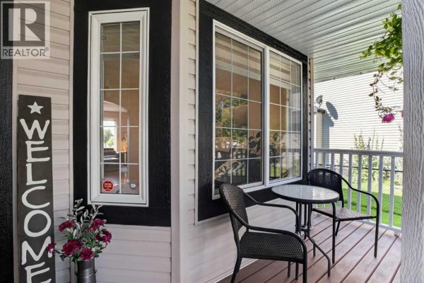 Covered front porch with a small table, two chairs, and a welcome sign. - 1713 High Park Drive Nw, High River