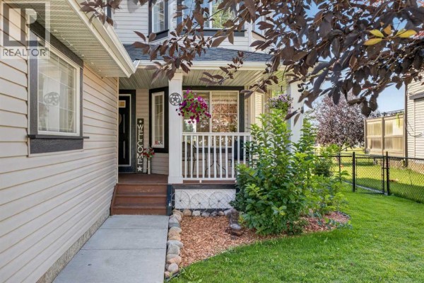 Front entrance of the house with a covered porch, wooden steps, and green lawn. - 1713 High Park Drive Nw, High River