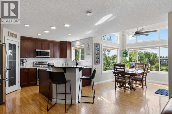 Open-concept kitchen and dining area with dark wood cabinets, white subway tile, and large windows. - 1713 High Park Drive Nw, High River