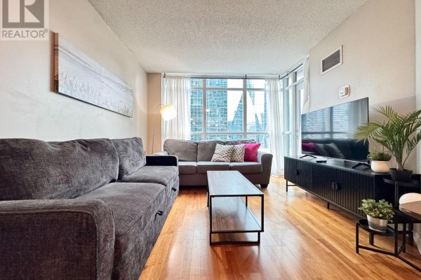 Spacious living room with two sofas, a coffee table, and a large window with city views. - 1715 - 18 Yonge Street, Toronto
