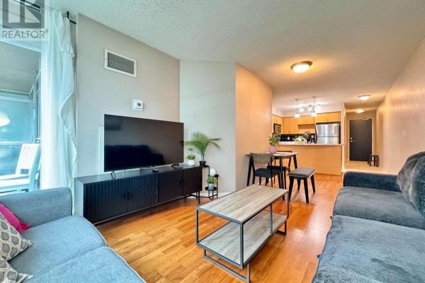 Living area with a sectional sofa, entertainment unit, and a view into the kitchen and dining space. - 1715 - 18 Yonge Street, Toronto