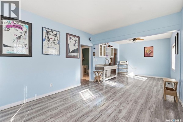 Living room with light blue walls, grey wood-look flooring, and an open doorway to another room. - 1715 Broadway Avenue, Saskatoon
