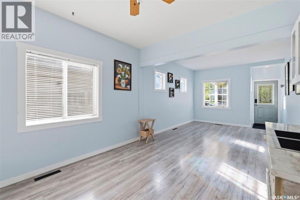Living room with light blue walls, grey wood-look flooring, windows, and a front door in the distance. - 1715 Broadway Avenue, Saskatoon