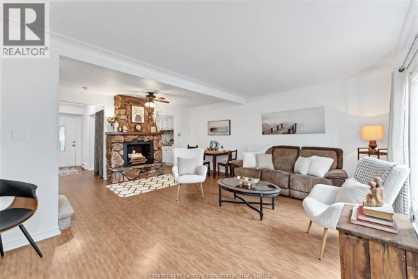 Living room with stone fireplace, wood floors, white walls, and large windows. - 1716 Eastgate Estates, Windsor