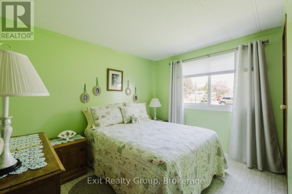 Bedroom with bright green walls, a queen bed with a floral quilt, and a window. - 172 - 63 Whites Road, Quinte West