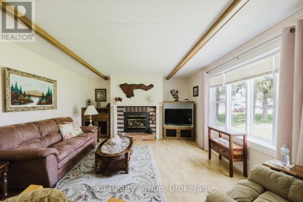 Living room with a brown sofa, fireplace with brick surround, and a large window. - 172 - 63 Whites Road, Quinte West