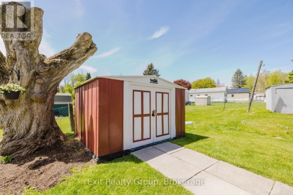 Red and white shed in a grassy yard next to a large, old tree. - 172 - 63 Whites Road, Quinte West