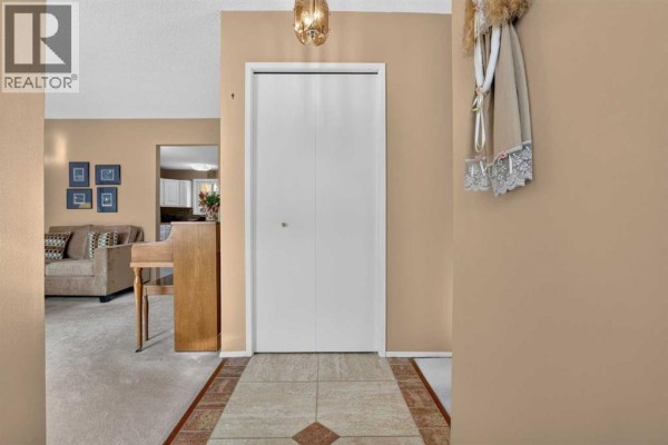 Interior hallway with beige walls, double white closet doors, and tiled floor with a patterned insert. - 172 Queensland Road Se, Calgary