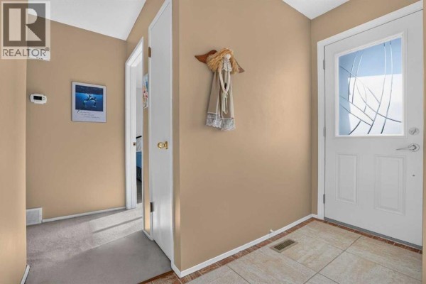 Hallway with beige walls, a white door with decorative glass, and a tiled entryway floor. - 172 Queensland Road Se, Calgary