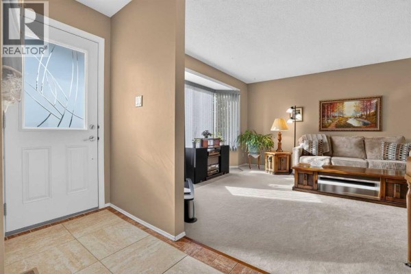 View from the hallway into a living room with beige carpet, sofa, and a bay window. - 172 Queensland Road Se, Calgary
