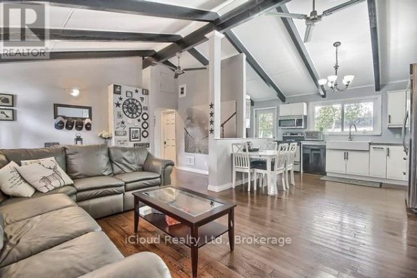 Open concept living room and kitchen with vaulted ceilings, exposed beams, a sectional couch, and dining table. - 172 Silas Boulevard, Georgina