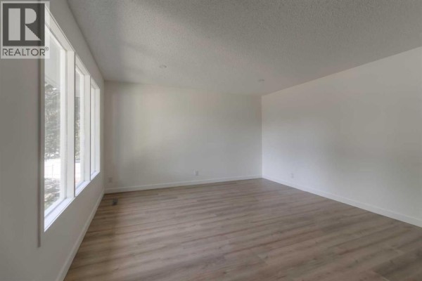 A spacious living room with white walls, large windows, and light wood laminate flooring. - 1721 2b Avenue N, Lethbridge