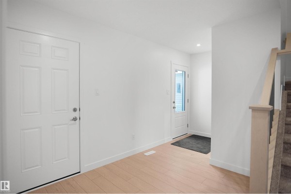 Interior hallway with light wood floors, white walls, two front doors, and a carpeted staircase with metal railings. - 1721 8 St Nw, Edmonton