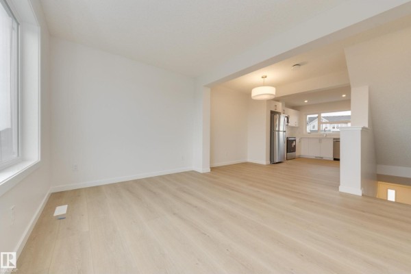 Spacious living area with light wood floors, white walls, and access to the kitchen and stairs. - 17226 4 St Nw, Edmonton