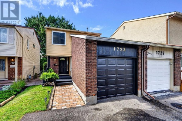 Front exterior of a townhouse with a paved walkway, green lawn, and mature trees. - 1723 Lafrance Drive, Ottawa
