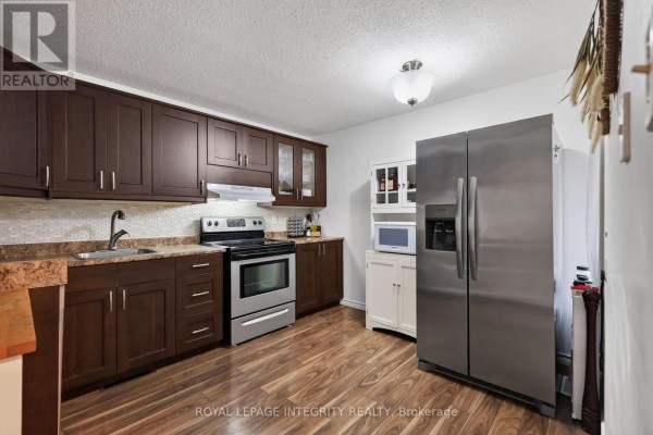 Kitchen with dark wood cabinets, stainless steel appliances, a microwave, and a stainless steel refrigerator. - 1723 Lafrance Drive, Ottawa