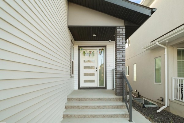Close-up of the front entrance with a glass door, concrete steps, and brick pillar. - 1724 19 St Nw, Edmonton