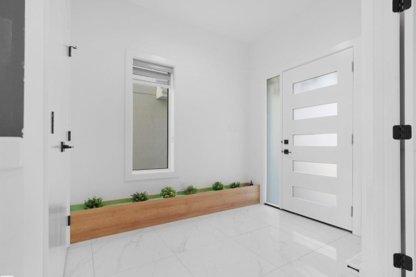Interior foyer with white walls, large white floor tiles, and a modern wooden planter. - 1724 19 St Nw, Edmonton