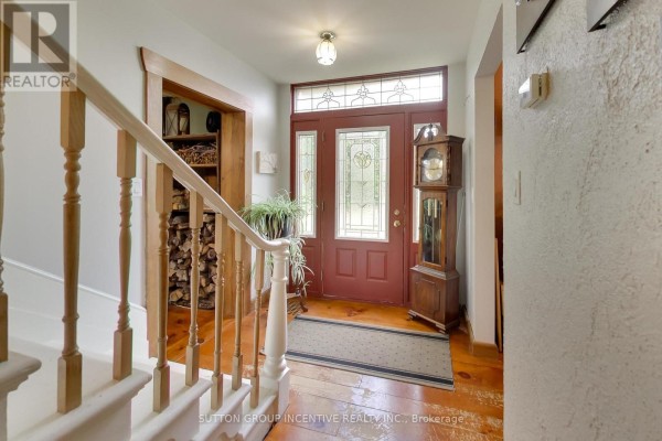 Interior foyer with a red front door, stained glass sidelights, wooden staircase, and grandfather clock. - 1724 Penetanguishene Road, Springwater