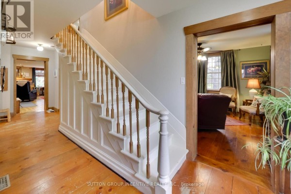 Interior hallway with a wooden staircase, leading to a living room with a fireplace and bay window. - 1724 Penetanguishene Road, Springwater
