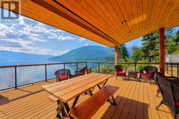 Wooden picnic table and chairs on a spacious wooden deck with a glass railing overlooking a lake. - 1726 31 Highway, Queens Bay