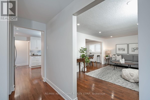 View from hallway into living room and kitchen area with wood floors. - 173 Arichat Road, Oakville