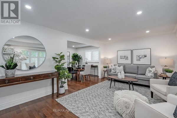 Living room with grey sofa, armchairs, coffee table, rug, and dining area beyond. - 173 Arichat Road, Oakville