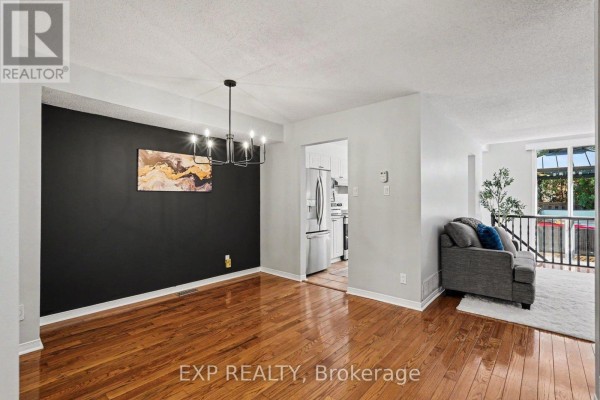 Dining area with hardwood floors, a dark accent wall, modern chandelier, and view into the kitchen. - 173 Beatrice Drive, Ottawa