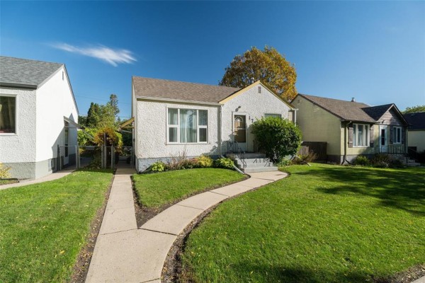 Side angle view of a white stucco house with a concrete sidewalk and lawn. - 173 Belmont Avenue, Winnipeg