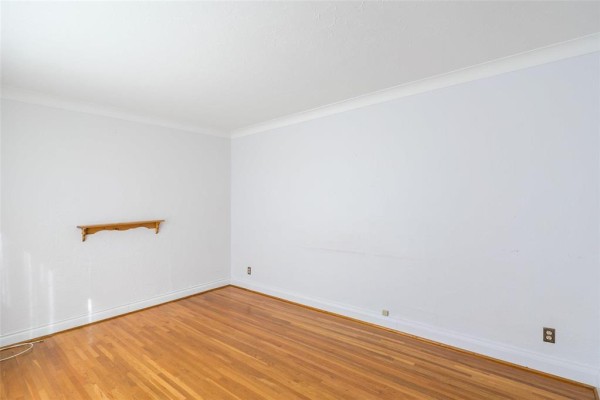 Empty room with light blue walls, hardwood floors, and a small wooden shelf on the wall. - 173 Belmont Avenue, Winnipeg