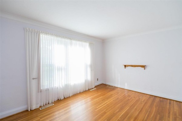 Empty room with light blue walls, hardwood floors, and large white curtains covering a window. - 173 Belmont Avenue, Winnipeg