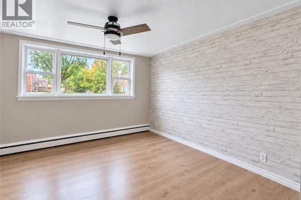 Bedroom with light wood floors, beige walls, a white accent wall, and a large window. - 173 Blucher Street Unit# 1, Kitchener