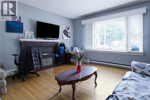 Living room featuring a brick fireplace, hardwood floors, and large windows. - 173 Maple Street, Moncton