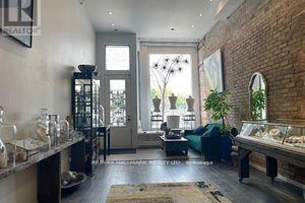 A retail space with exposed brick walls, display cases, a teal sofa, and large windows. - 173 Queen Street E, Toronto