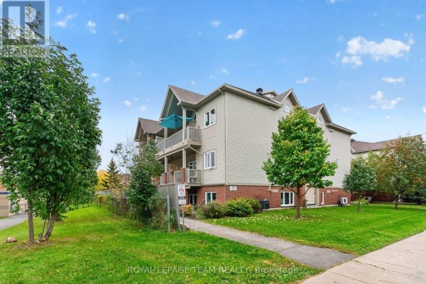 Side view of apartment building with beige siding and brick base, bordered by trees and lawn. - 173-c Crestway Drive, Ottawa