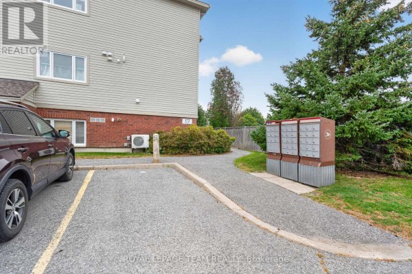 Parking area with gravel surface and mailboxes, next to apartment building with dark brown car. - 173-c Crestway Drive, Ottawa