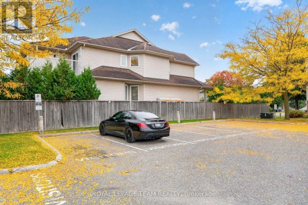 Apartment building exterior with beige siding and wooden fence, featuring a black sedan in a parking space. - 173-c Crestway Drive, Ottawa