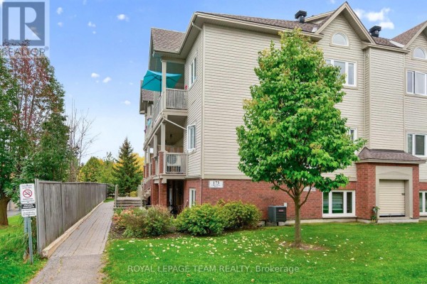 Apartment building exterior with beige siding and brick base, featuring balconies and a mature tree. - 173-c Crestway Drive, Ottawa