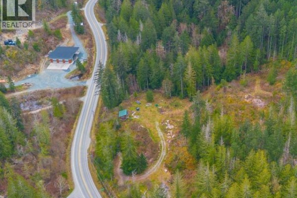 View of Highway 101 winding past a modern building and a wooded hillside with a small green structure. - 1731 Highway 101, Powell River