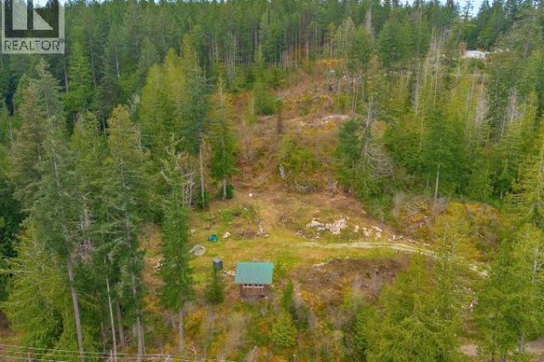 Close-up aerial view of a small green-roofed structure nestled among trees on a sloped, wooded lot. - 1731 Highway 101, Powell River
