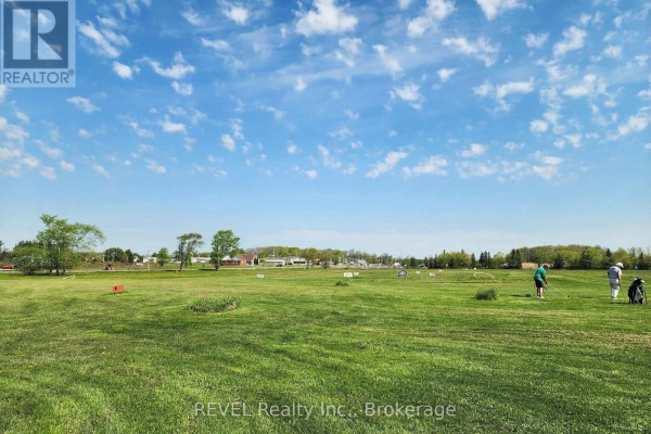 Wide view of a green golf driving range with people practicing and markers. - 1732 Merrittville Highway, Thorold