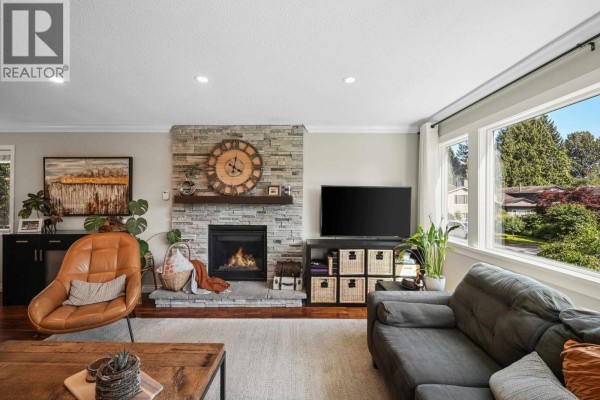 Living room fireplace with stone surround, television, and view of backyard. - 1737 Anderson Way, Port Coquitlam