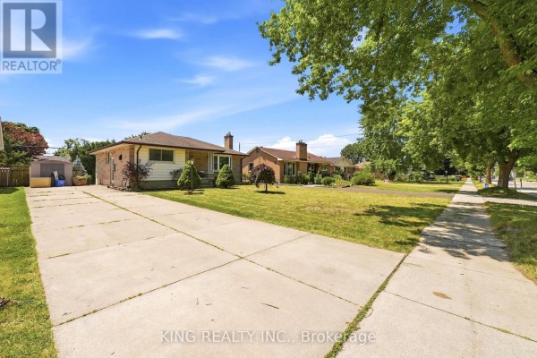 Long driveway leading to a single-story house with a concrete sidewalk and mature trees. - 1737 Wavell Street, London East