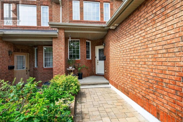 Front exterior of brick townhouse with paved walkway and green landscaping. - 174 Carwood Circle W, Ottawa