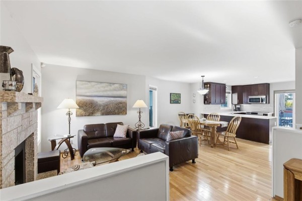 Living room with leather sofas, stone fireplace, and view of dining area. - 174 Foxmeadow Drive, Winnipeg