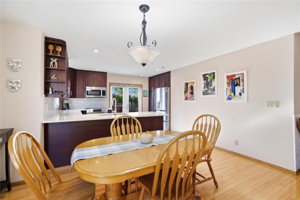 Dining area with oval wood table, chairs, and view of kitchen island. - 174 Foxmeadow Drive, Winnipeg