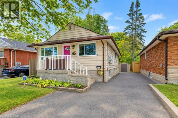Side exterior view of the beige bungalow showing the driveway, a storage shed, and adjacent brick house. - 174 Glen Road, Kitchener